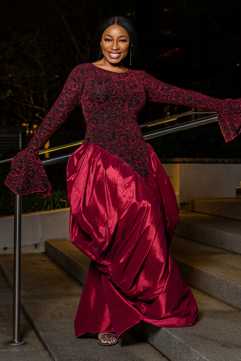 A woman wearing a long-sleeve burgundy and black lace top with a matching shiny satin skirt, posing on outdoor stone steps at night.