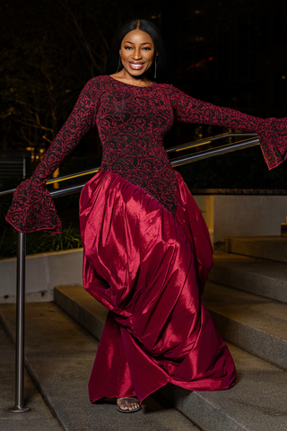 A woman wearing a long-sleeve burgundy and black lace top with a matching shiny satin skirt, posing on outdoor stone steps at night.