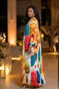 Woman in a colorful floral dress standing outdoors with warm lighting.