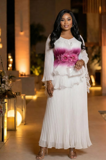 Woman in a white dress with a floral pink design in the middle standing in an elegant indoor setting.