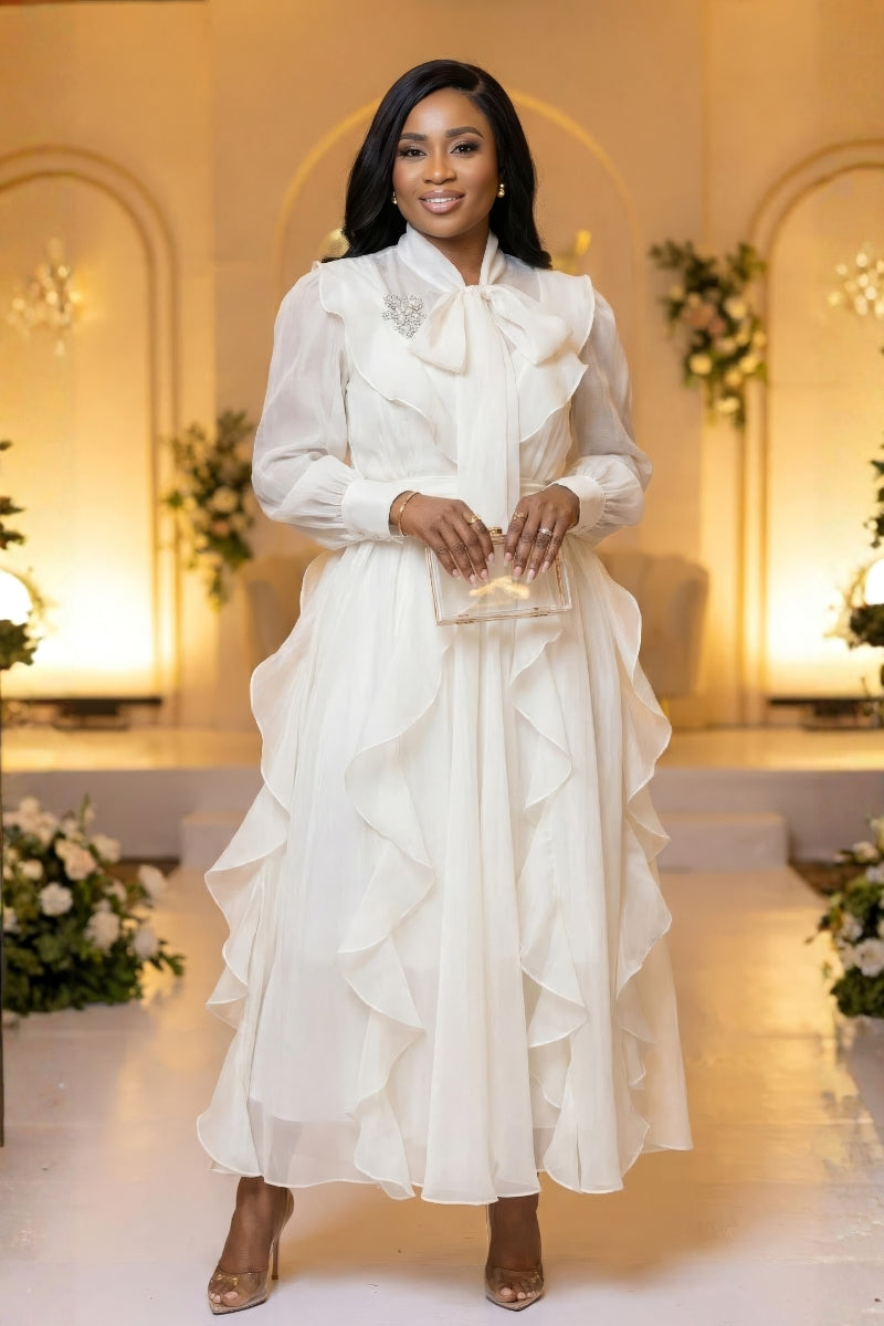 Woman in a white dress standing in an elegant indoor setting with floral decorations.