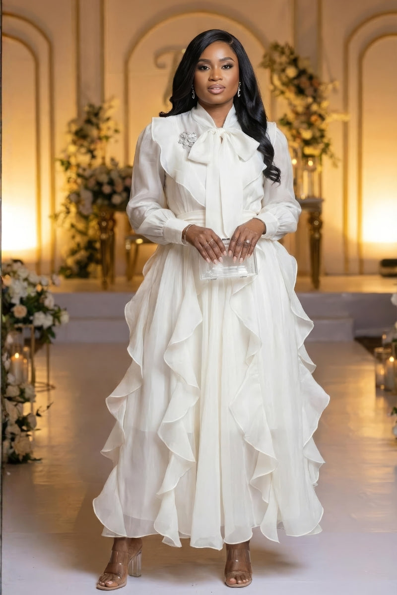 Woman in a white dress standing in an elegant indoor setting with floral decorations.