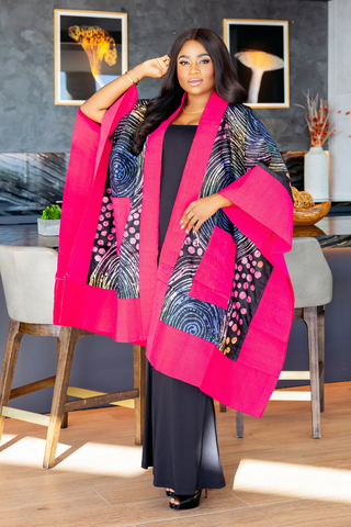 A woman modeling a vibrant hot pink and black patterned shawl draped over her shoulders, worn over a black dress in a modern kitchen setting.