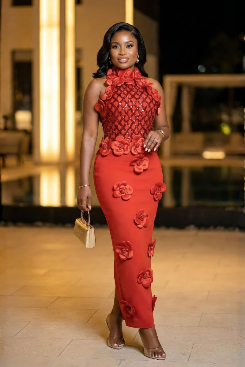Woman in a red dress with floral patterns standing outdoors at night.