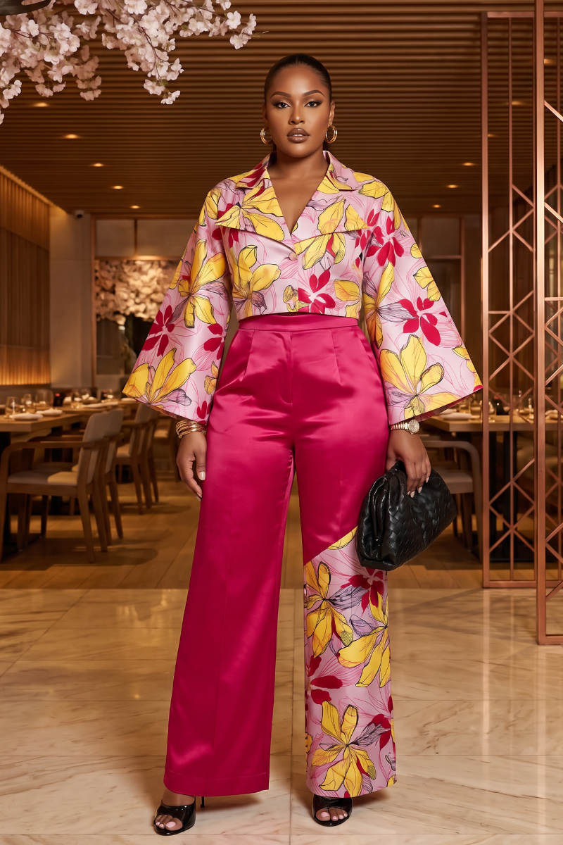 Woman in a colorful floral blouse and pink pants standing in an elegant interior setting.
