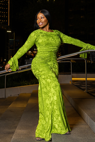 A woman posing in a vibrant lime green lace long-sleeve mermaid gown on outdoor steps at night.