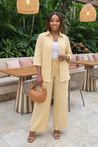 Woman in a yellow outfit standing in an outdoor setting with tables and chairs.