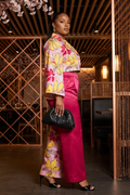 Woman in a colorful outfit with pink pants and floral top standing in an indoor setting.
