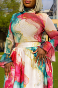 A woman wearing a long-sleeve high-neck dress with a colorful abstract marble print in pink, teal, cream, and gold, photographed outdoors on a grassy lawn.