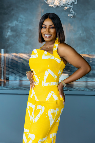 Woman in a yellow dress with white patterns posing against a blurred indoor background