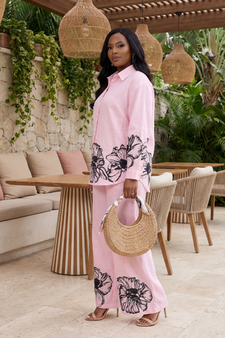 Woman in a pink outfit with floral patterns standing in an outdoor setting.
