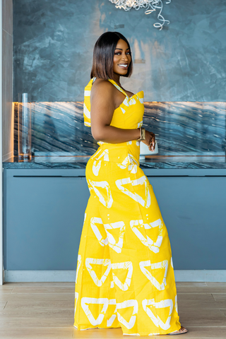 Woman in a yellow dress with white patterns standing indoors against a blue wall.