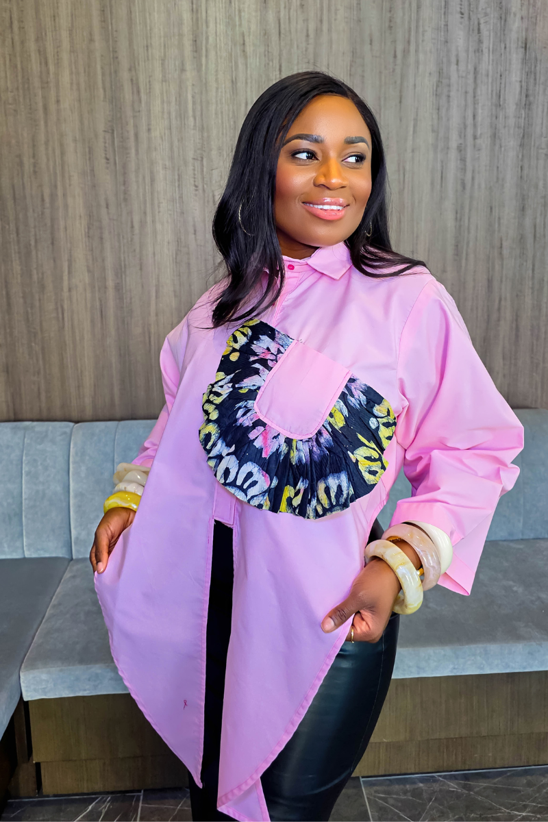 Woman wearing a white blouse with a colorful design and brown leather skirt in an indoor setting.