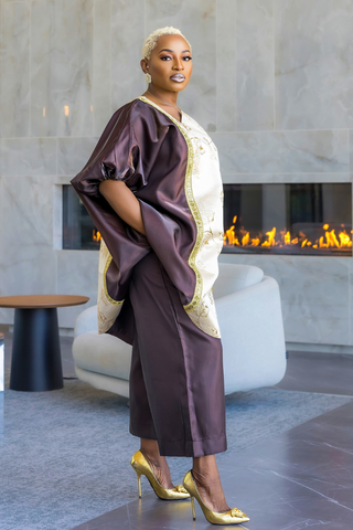 A woman models a two-piece satin outfit featuring a dark brown tunic with gold embroidery and wide sleeves, paired with matching brown wide-leg pants, set against a modern interior with a fireplace.