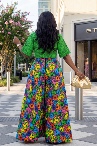 Woman in a green top and colorful floral pants walking outdoors near a store entrance.