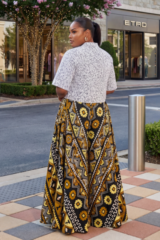 Woman wearing a patterned skirt and blouse on a city street with 'Etro' store in the background.
