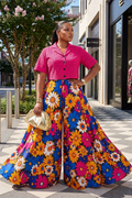Woman in a colorful floral dress and pink top standing on a city street.