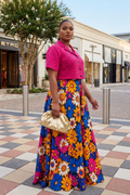 Woman in a colorful floral dress and pink top standing on a city street.