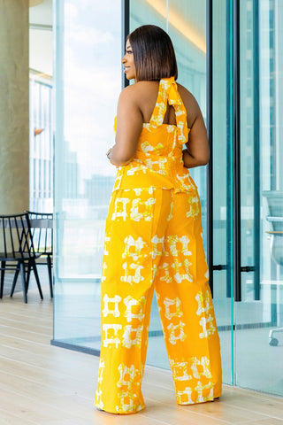 Woman wearing a yellow and white patterned jumpsuit standing in a modern indoor setting.