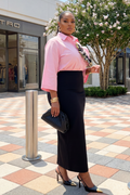 Woman in pink blouse and black skirt standing on a sidewalk with a store in the background