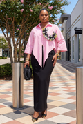 Woman in a pink shirt and black pants standing on a sidewalk with shops in the background.