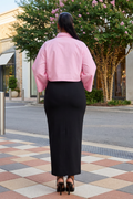 Person wearing a pink shirt and black skirt on a city street.