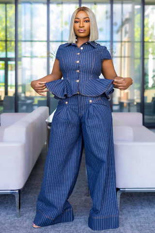 A woman modeling a blue pinstriped short-sleeve button-up shirt and matching wide-leg pants in a modern office lobby setting.