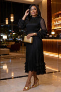 Woman in a black dress with ruffled sleeves and gold shoes in a hotel lobby.