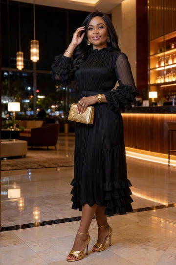 Woman in a black dress with ruffled sleeves and gold shoes in a hotel lobby.