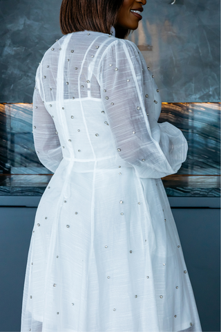 Woman wearing a white dress with long sleeves and embellishments in front of a blurred background