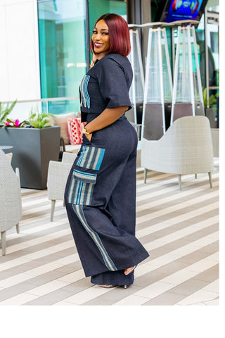 Woman in a stylish outfit standing in an indoor setting with chairs and plants.