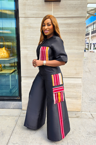 A woman wearing a black asymmetric crop top and tailored pants with geometric patterns on the pockets, standing outdoors.