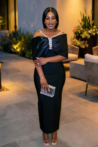 Woman in a black off-shoulder dress with white embellishments standing outdoors.