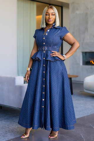 A woman models a blue pinstriped maxi dress with a button-down front, short sleeves, and a peplum waist in a modern indoor setting.
