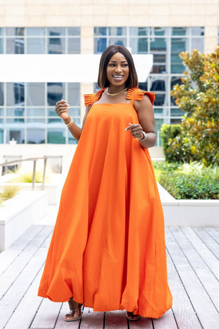 Woman wearing an orange dress with ruffled straps outdoors.