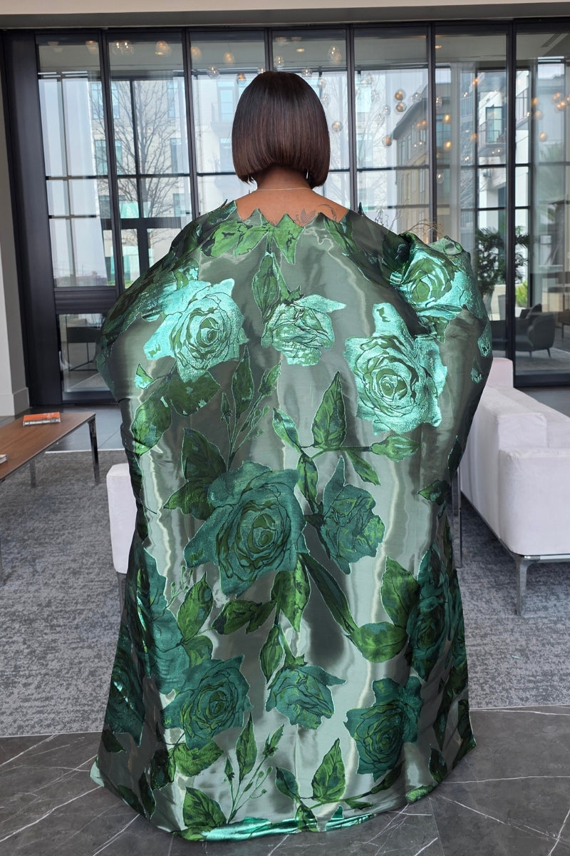 Woman in a green floral dress standing in an indoor setting with modern decor.