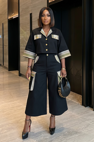 Woman in stylish black outfit with gold accents standing indoors.