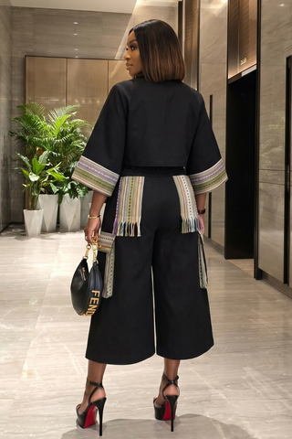Woman in a stylish outfit with a black top and wide-leg pants, holding a handbag, in an indoor setting.