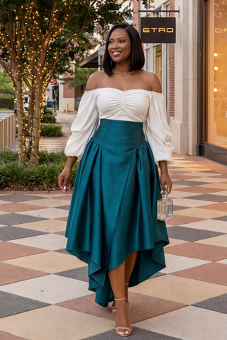 Woman in a white top and teal skirt standing on a patterned sidewalk with a store sign in the background.