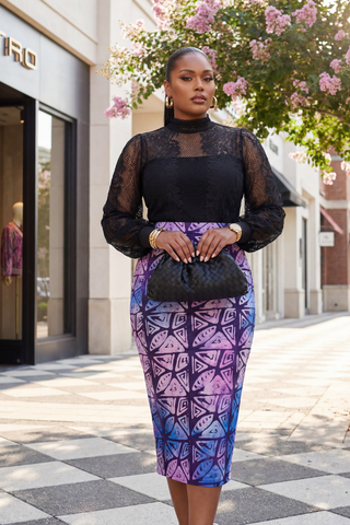 Woman in a black top and colorful skirt standing on a city street.