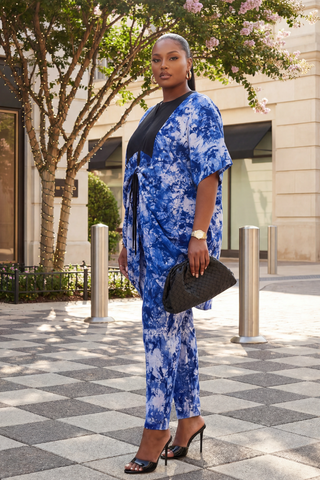 Woman in a blue tie-dye outfit standing on a city street.