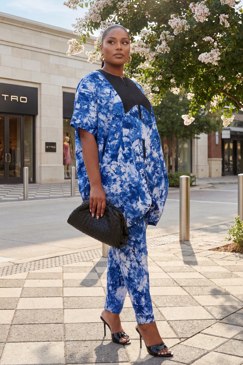 Woman wearing a blue tie-dye outfit with black top and pants, holding a black clutch, on a city street.