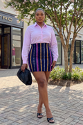 Woman in a pink shirt and striped skirt standing on a sidewalk with shops in the background