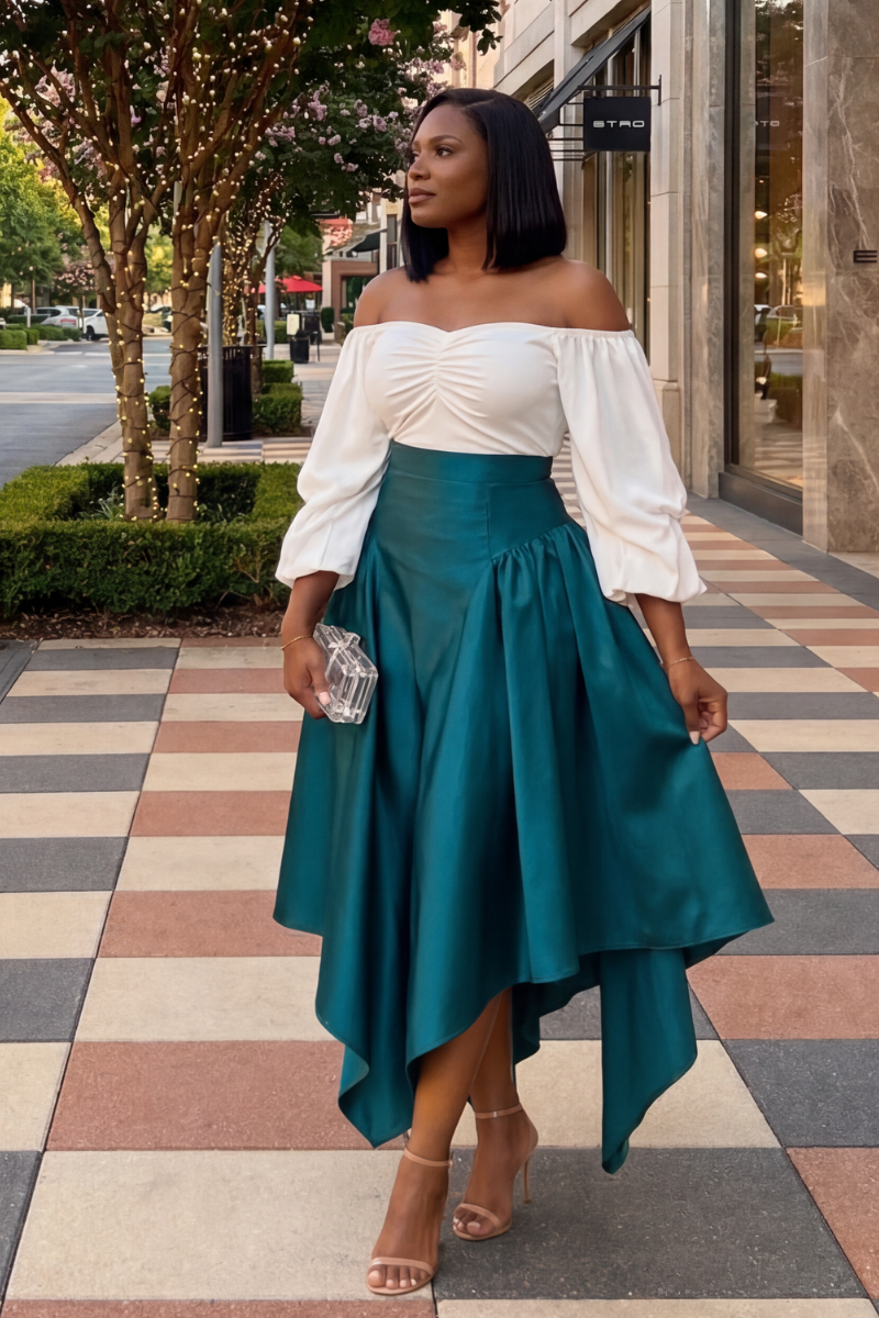 Woman in a white top and teal skirt standing on a sidewalk with trees and buildings in the background.