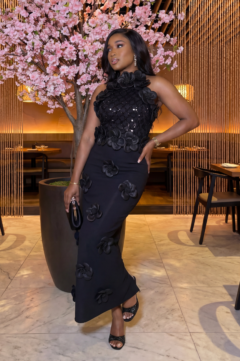 Woman in a black floral dress standing in a restaurant setting with pink floral decorations.
