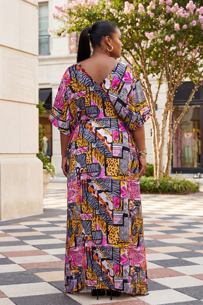 Woman wearing a colorful patterned dress standing outdoors near a building with pink flowers.