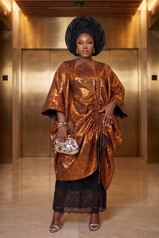 Woman in a bronze outfit with a black headwrap standing in a gold-colored room.
