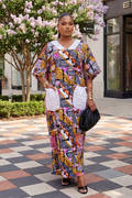 Woman in colorful patterned outfit standing outdoors with a building and tree in the background