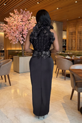 Woman in a black evening gown with floral details walking through a restaurant.