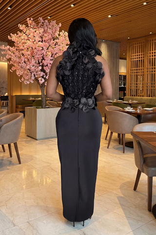 Woman in a black evening gown with floral details walking through a restaurant.